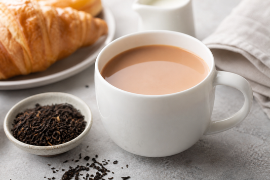 A white mug of English Breakfast tea on a table with loose black tea leaves nearby