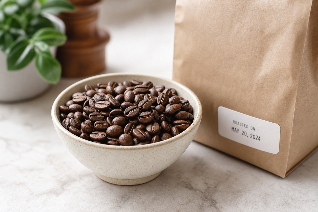 Fresh roasted coffee beans beside a coffee bag with a roast date label on a counter